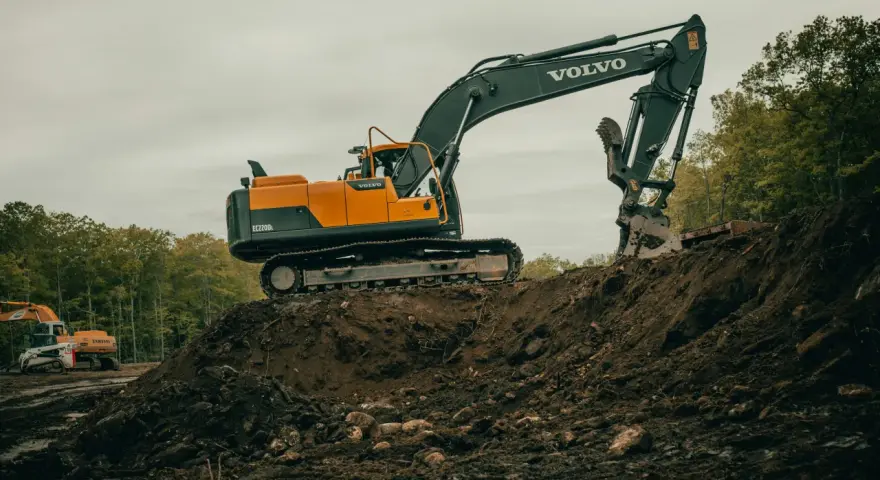 Pomarańczowo-czarna koparka Volvo EC220DL pracuje na budowie. Operator koparki gąsienicowej zarabia dobrze, wykonując ciężką pracę.