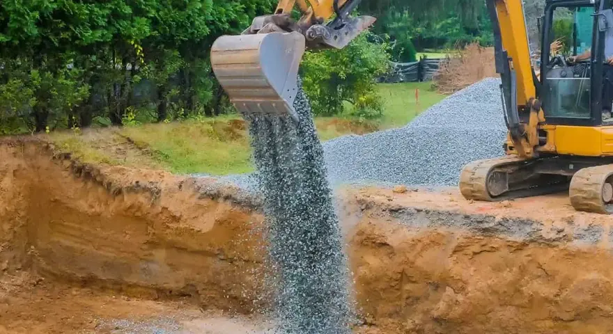 Koparka wysypuje tłuczeń do wykopu, tworząc fundament pod przyszłą drogę.