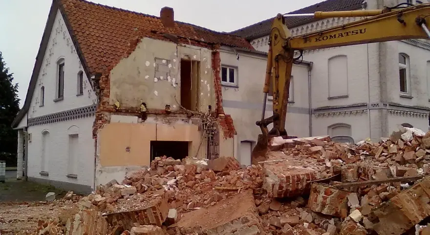 Rozbiórka budynku w granicy działki. Koparka Komatsu pracuje przy gruzach.