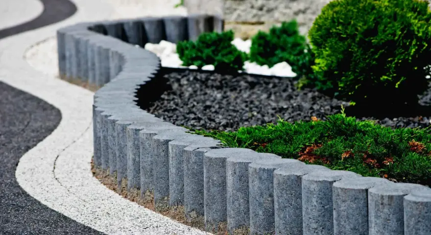 Obrzeże z kostki granitowej tworzy falistą linię, oddzielając ścieżkę od zadbanej rabaty z iglakami i kamieniami.