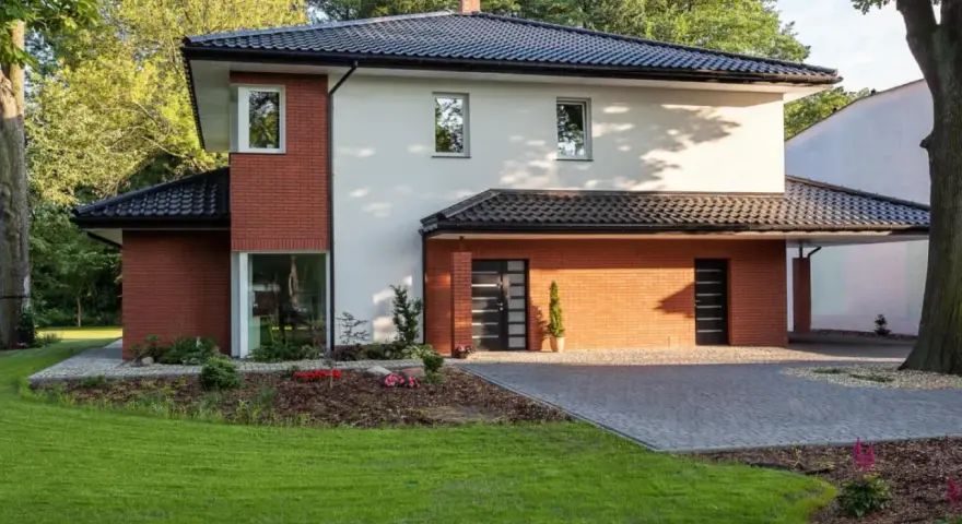 Nowoczesny dom z ceglanymi akcentami i eleganckim, czarnym dachem czterospadowym, otoczony zielenią.