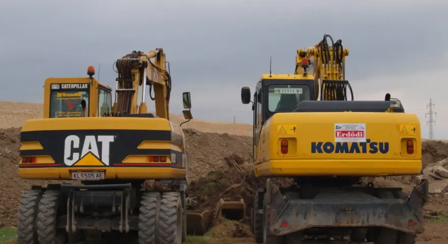Dwie żółte koparko-ładowarki, CAT i Komatsu, stoją na placu budowy. Czy koparko ładowarka musi być zarejestrowana?