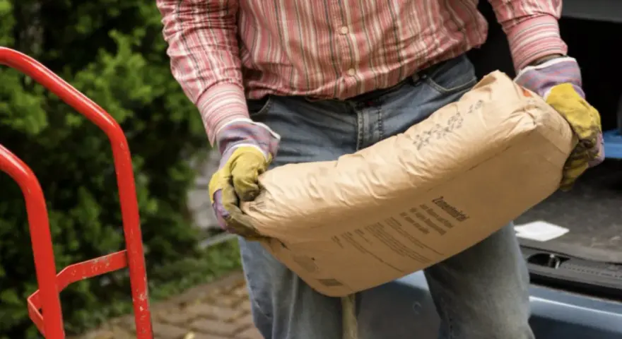Mężczyzna w rękawicach niesie worek cementu, zastanawiając się, ile cementu do piasku potrzeba do zaprawy.