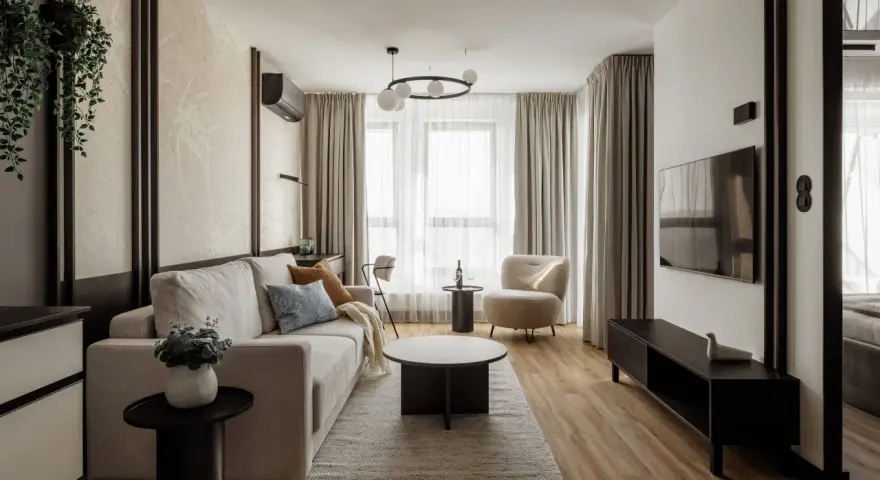 Nowoczesny salon z beżową kanapą, fotelem i telewizorem.