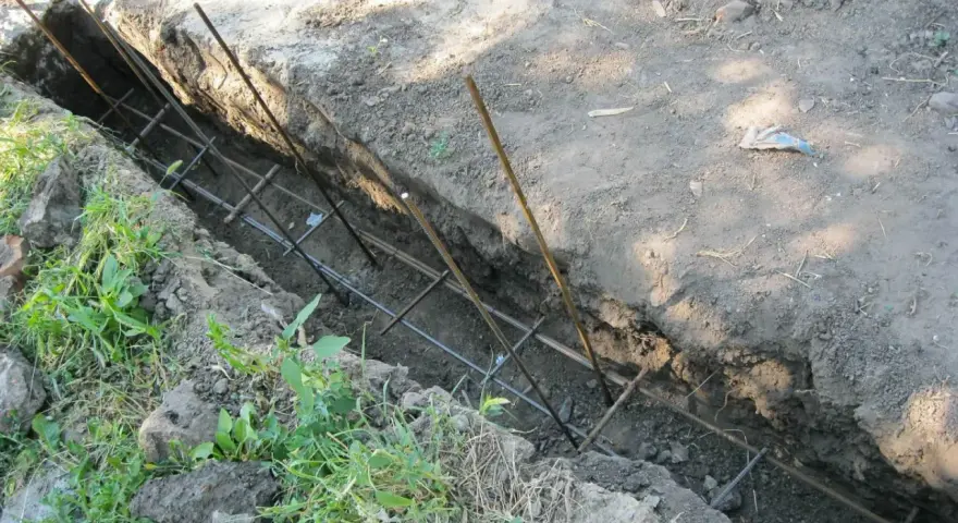 Wykonanie fundamentu pod ogrodzenie. W wykopie widoczna zbrojenie z prętów stalowych, gotowe do zalania betonem.