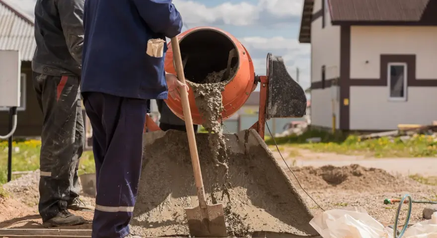 Pracownicy budowlani wylewają beton z betoniarki. Pytanie: ile cementu na betoniarkę 200?