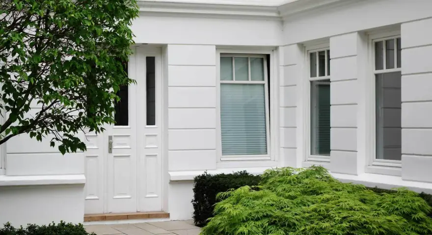 Boniowanie elewacji domu podkreśla jego klasyczny charakter. Białe drzwi i okna, otoczone zielenią, tworzą elegancką całość.