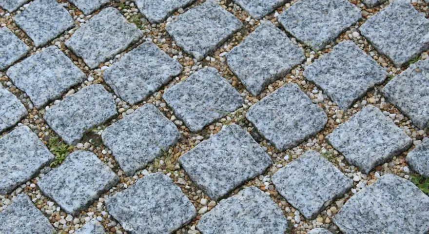 Szara kostka granitowa ułożona na podsypce. Widać, ile podsypki pod kostkę na m2 jest potrzebne do stabilnego ułożenia.