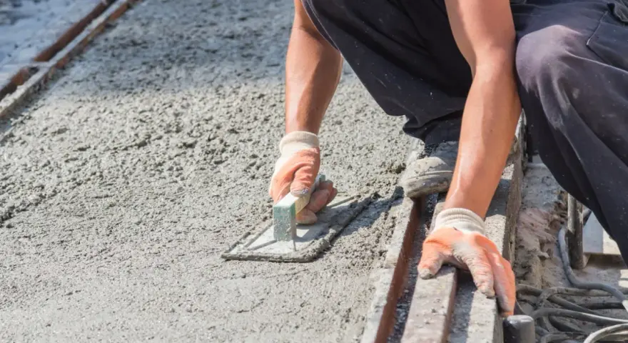 Pracownik w rękawicach wygładza świeży beton kielnią. To kluczowy etap, jak zrobić suchy beton, by był równy i trwały.