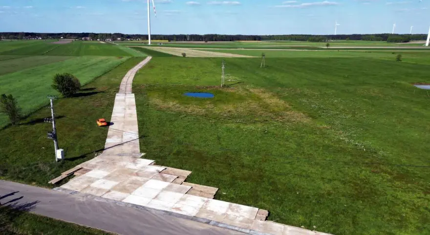 Teren budowy farmy wiatrowej z tymczasową drogą z płyt betonowych. Tłuczeń na drodze ułatwia dojazd ciężkiego sprzętu.
