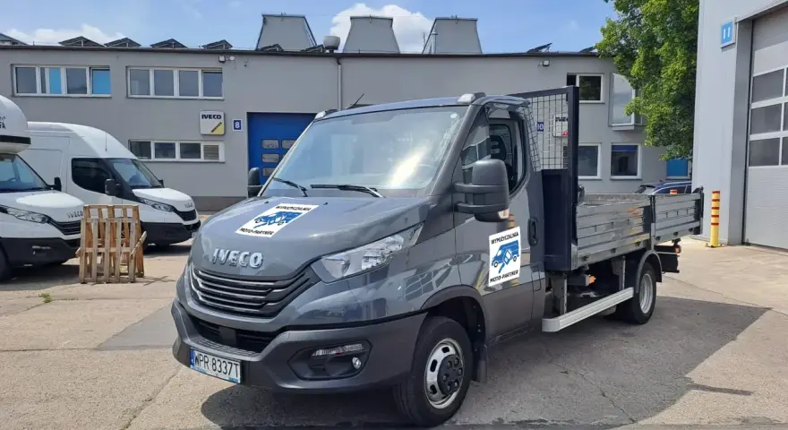 Szary Iveco z otwartą skrzynią ładunkową, idealny do wynajem wywrotki do 3,5 tony. Na drzwiach logo "Wypożyczalnia Moto-Partner".