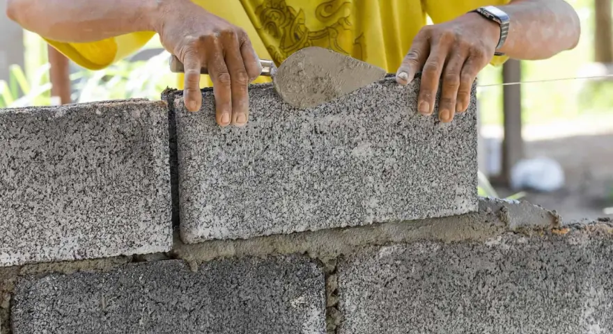 Budowniczy układa kostkę fundamentową na zaprawie.