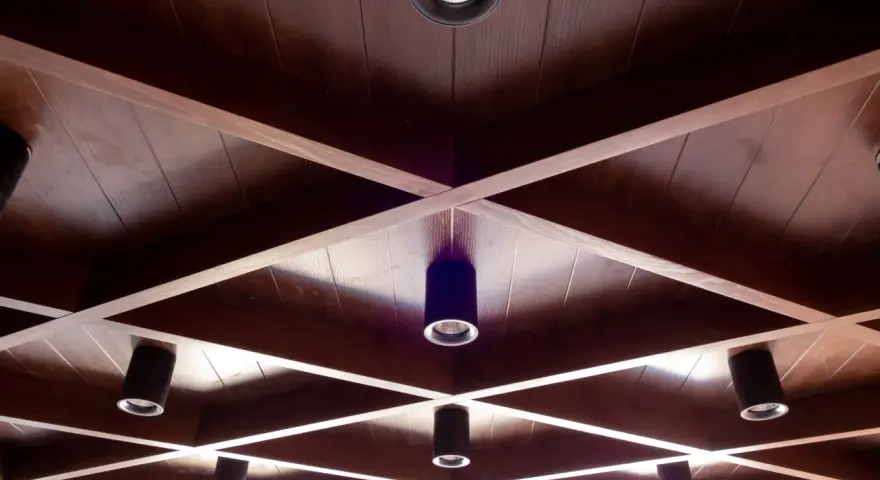 Drewniane, kratownicowe **stare kasetony na suficie** z wbudowanymi reflektorami tworzą geometryczny wzór.