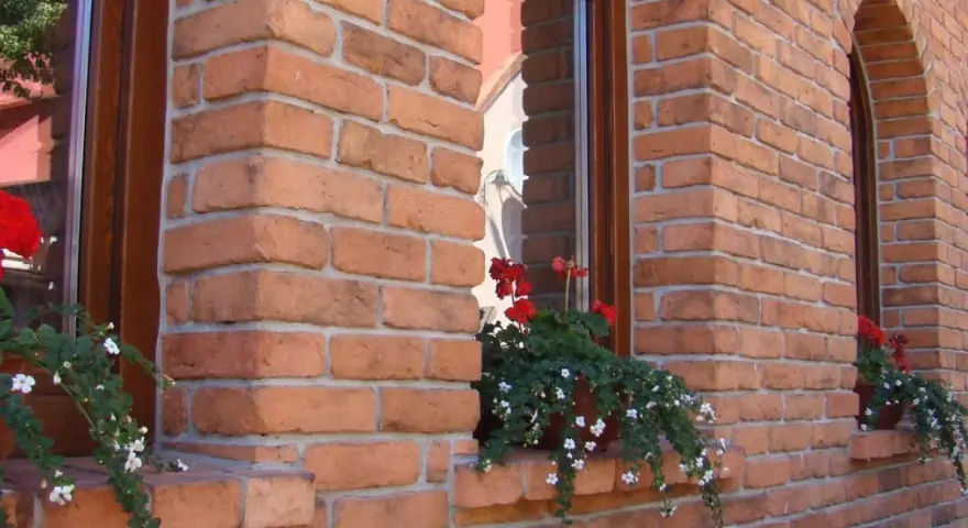 Elegancka elewacja z cegły klinkierowej, z kwitnącymi pelargoniami przy oknach. Sprawdź, jaka jest cegła klinkierowa cena!