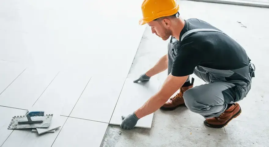 Fachowiec układa płytki na balkonie. Dowiedz się, ile kosztuje położenie płytek na balkonie i jakie materiały są potrzebne.
