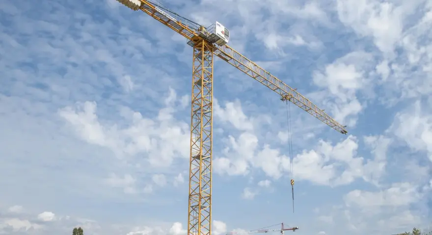 Żółty dźwig budowlany na tle błękitnego nieba z chmurami. Zastanawiasz się, ile zarabia operator dźwigu?