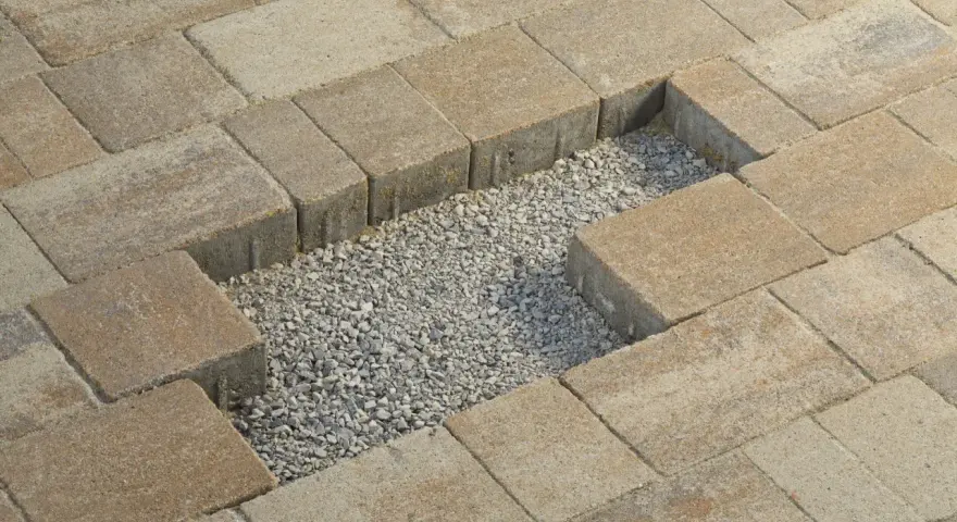 Fragment kostki brukowej z widocznym wycięciem i żwirem. Wiercenie w kostce brukowej jest w trakcie.