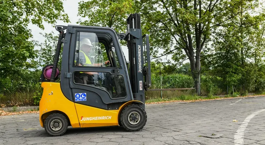 Operator w kasku i kamizelce prowadzi wózek widłowy Jungheinrich. Zastanawiasz się, ile kosztuje uprawnienia na wózek widłowy?