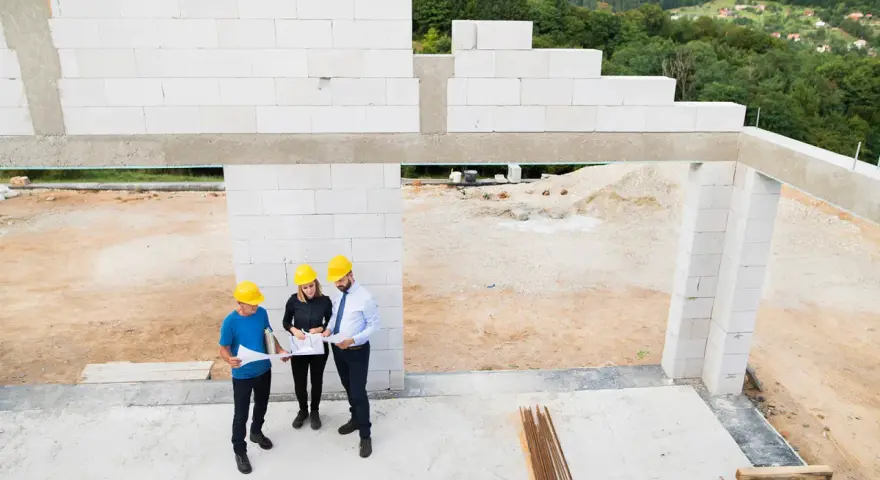 Architekci omawiają projekt domu z bloczków silikatowych. Budowa w toku, w tle zielone wzgórza.