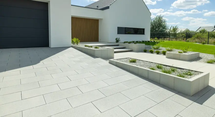 Nowoczesne wzory kostki brukowej przed domem tworzą schludny podjazd i ścieżki, otoczone geometrycznymi rabatami.