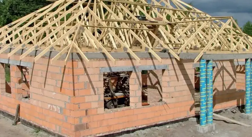 Budowa domu z cegły, na którym widać drewnianą konstrukcję dachu kopertowego.