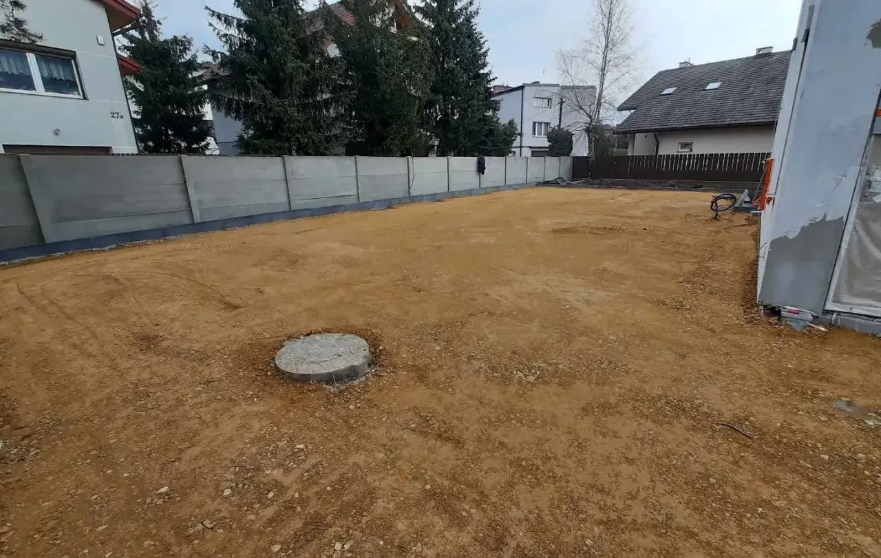 Gotowy teren po przygotowaniu podłoża pod kostkę. Widać betonowe płyty ogrodzenia i okrągły właz.