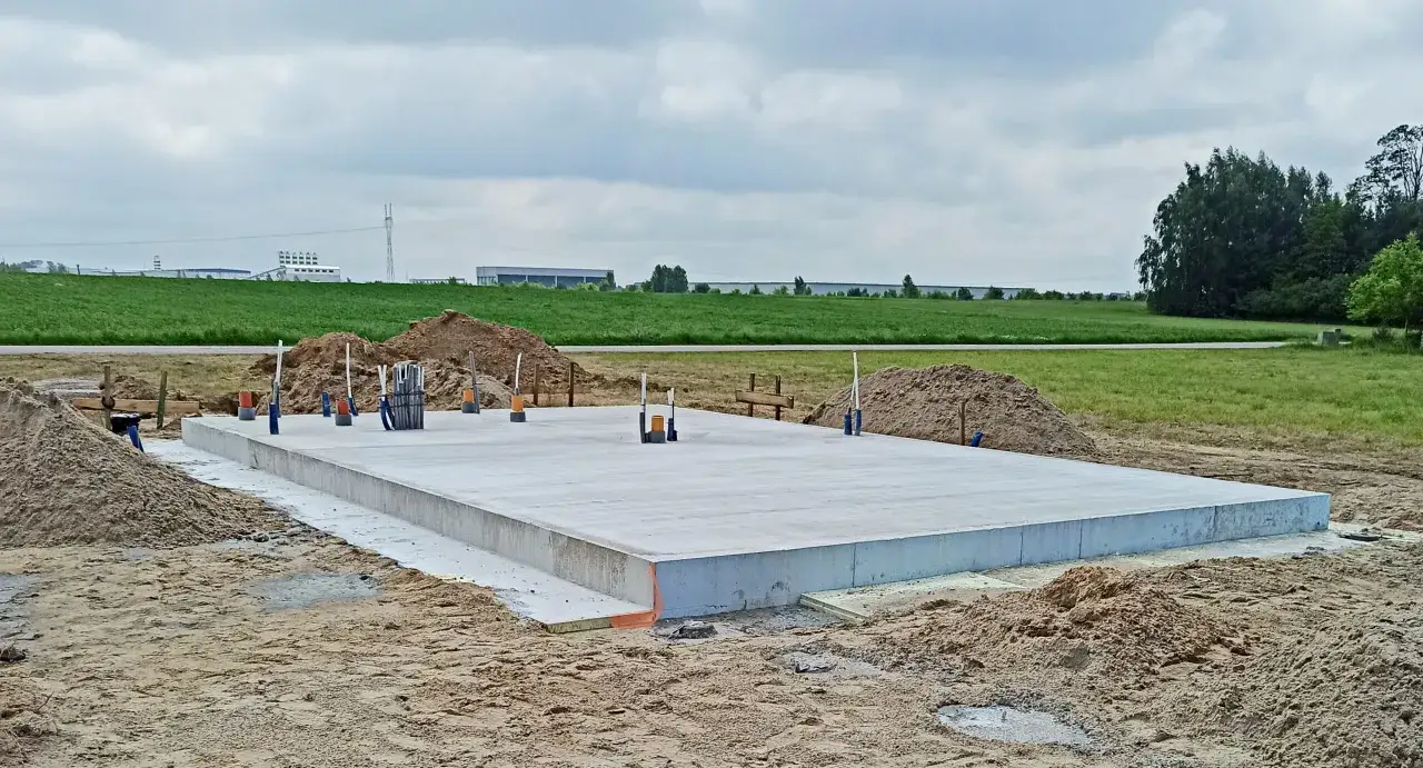 Gotowy fundament pod budowę domu, wykonany po wymianie gruntu pod płytę fundamentową. Wokół plac budowy.