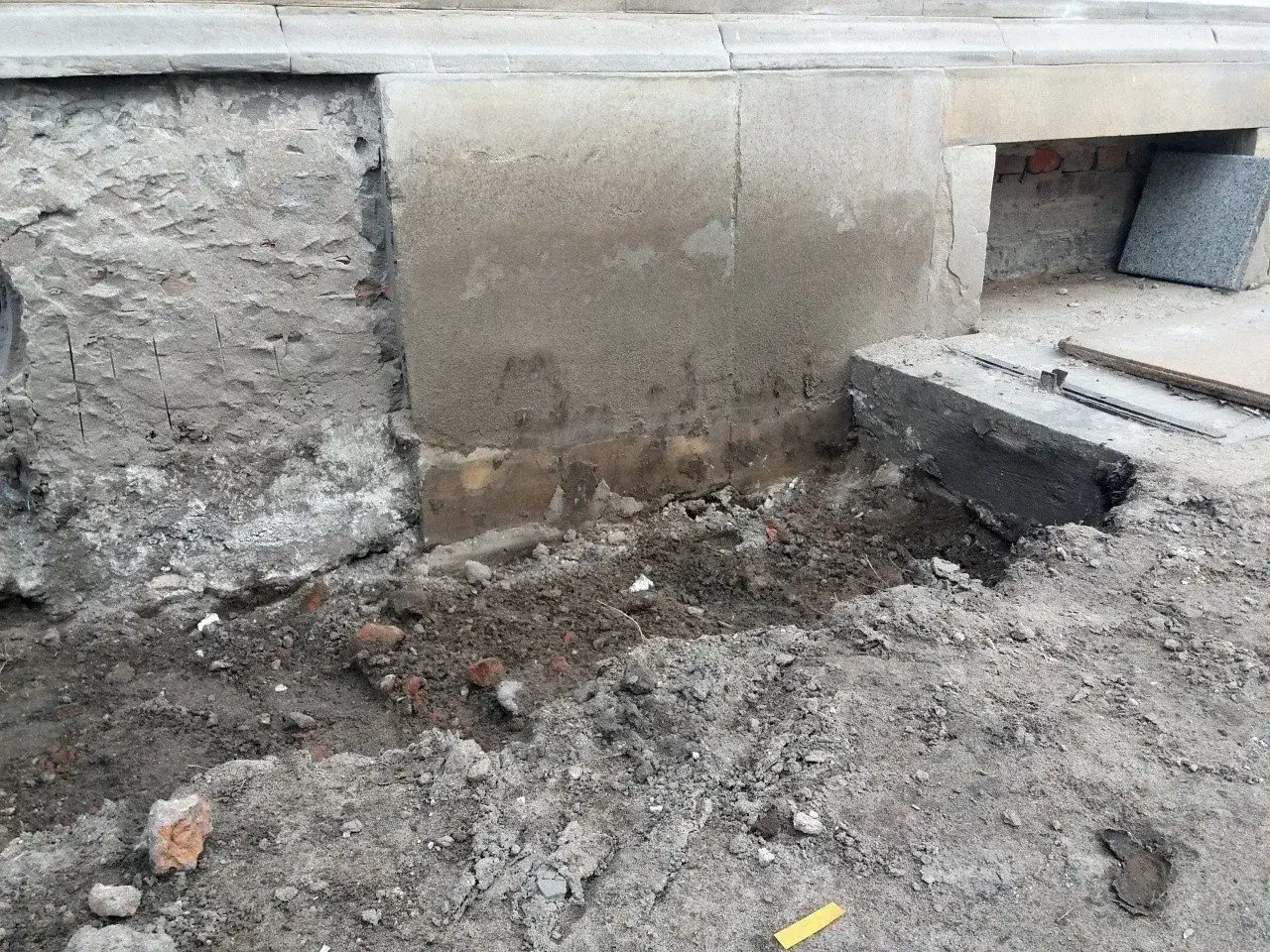Prace przy fundamencie. Widać odsłoniętą, starą cegłę i ziemię. Czekamy, aż fundamenty odstać.