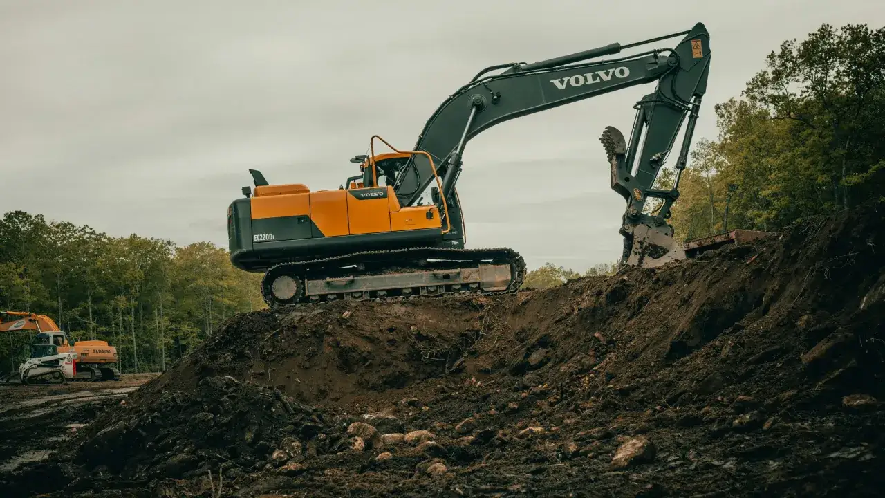 Pomarańczowo-czarna koparka Volvo EC220DL pracuje na budowie. Zastanawiasz się, ile zarabia operator koparki gąsienicowej?