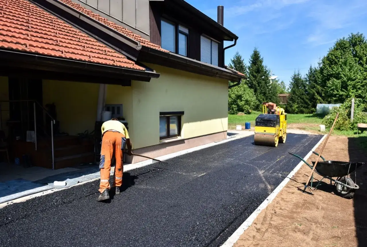 Pracownik równa asfalt, a walec go zagęszcza. Zastanawiasz się, ile kosztuje asfalt za m2?