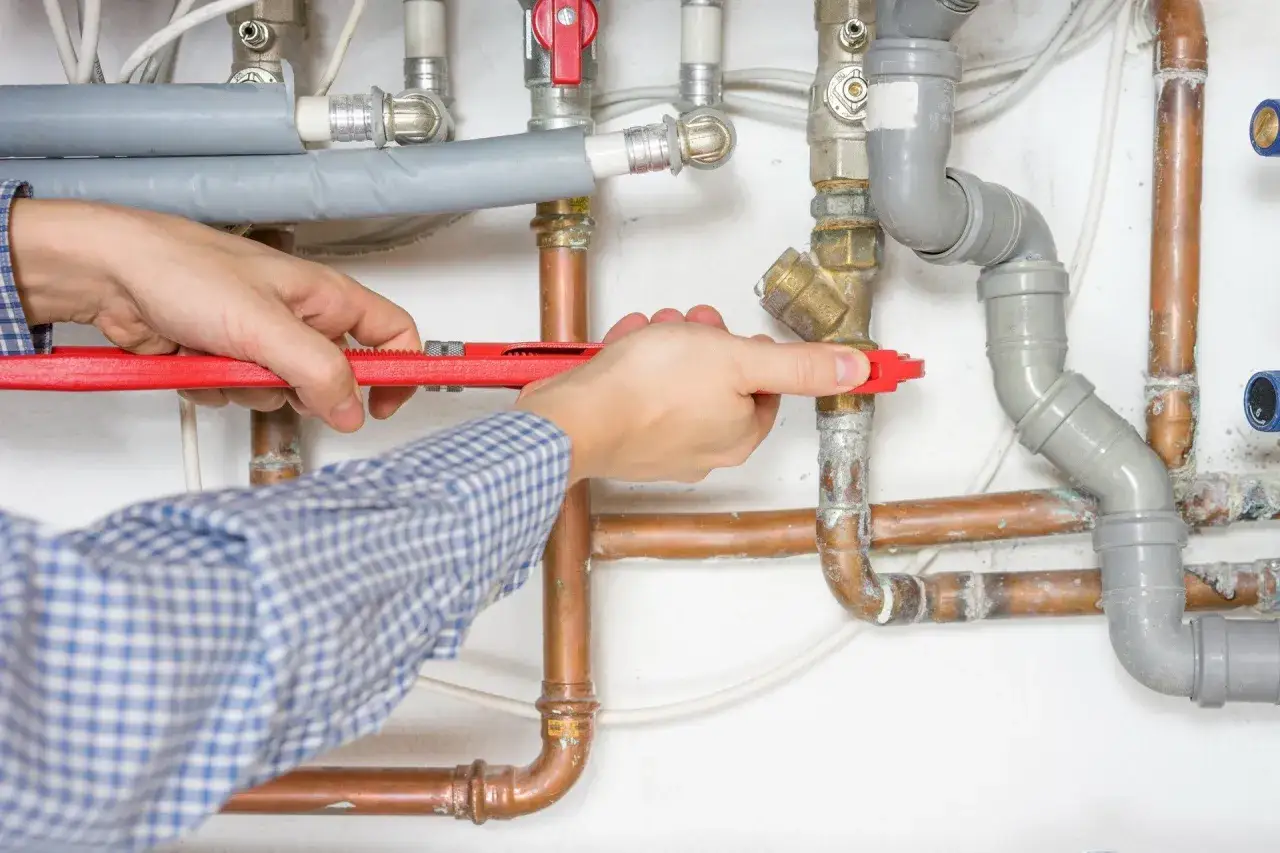 Ręce majstra przykręcają rury kluczem. Zastanawiasz się, ile kosztuje hydraulik?