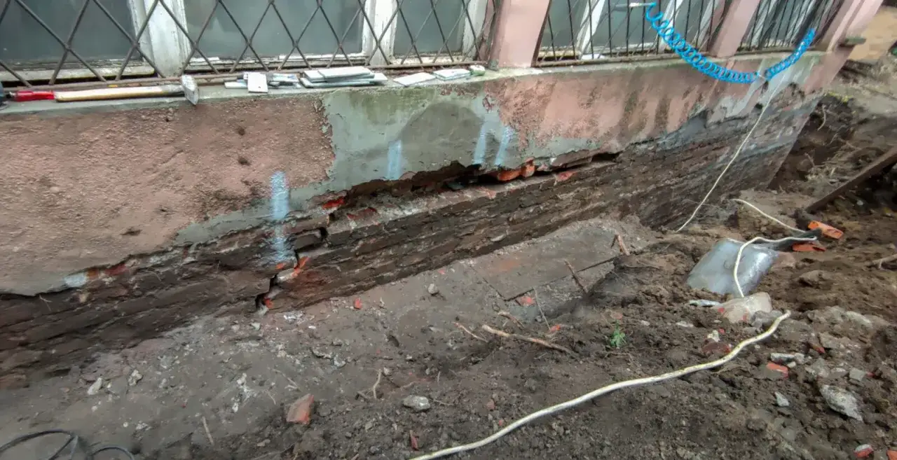 Odsłonięta, zniszczona ceglana podmurówka budynku, wokół wykopana ziemia. Czekamy, aż fundamenty odstać.