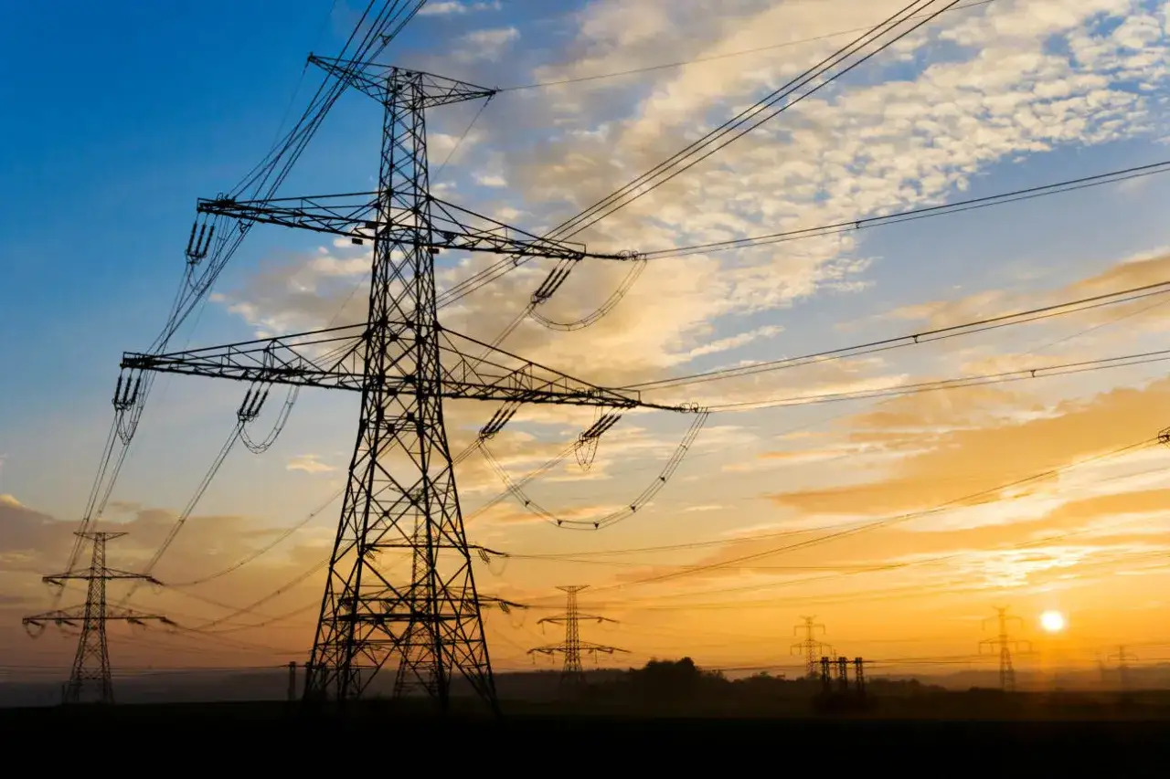 Wieże energetyczne na tle zachodzącego słońca. Pamiętaj o zachowaniu bezpieczna odległość od linii energetycznych.