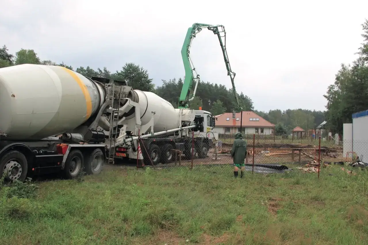Betoniarka z wysięgnikiem pompy do betonu przygotowuje się do pracy. Zastanawiamy się, ile żwiru na worek cementu potrzeba do budowy domu w tle.